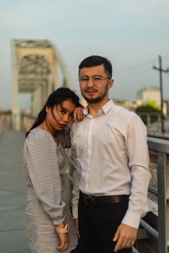 A vertical shot of a couple standing on an old bridge on a windy day in Saigon, Vietnam