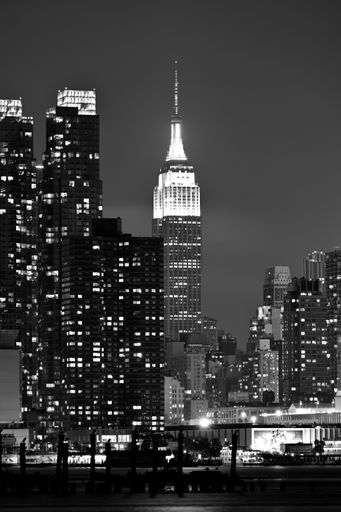 A vertical grayscale shot of a cityscape with illuminated buildings