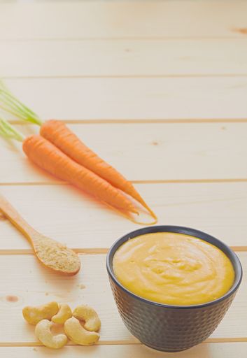 A vertical shot of pudding in a black bowl with carrots cashew nuts and sesame seeds on a wooden table