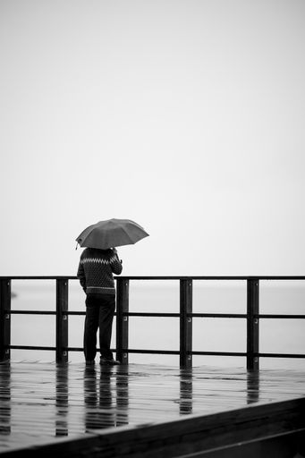 A vertical back view of a person with an umbrella enjoying a rainy day on the pier