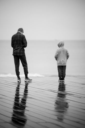 A vertical back view of a father and his child enjoying a rainy day on a pier