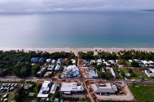 Aerial view of a coastal town with lush greenery and calm ocean waters under a cloudy sky, capturing a serene and tranquil atmosphere.