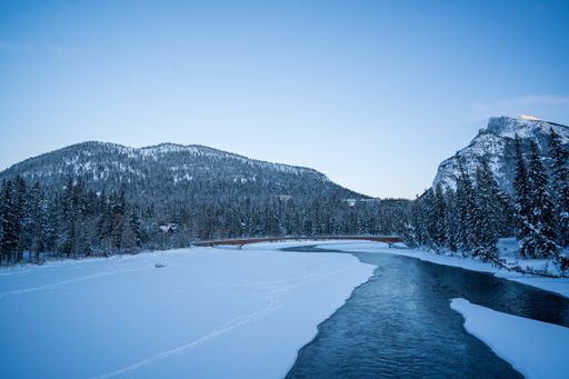 A chilling view of a frozen river and forest landscape under a clear blue sky