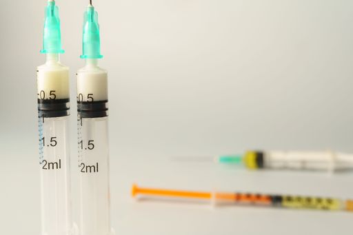 Two syringes containing a milky substance are in focus, with other filled syringes blurred in the background