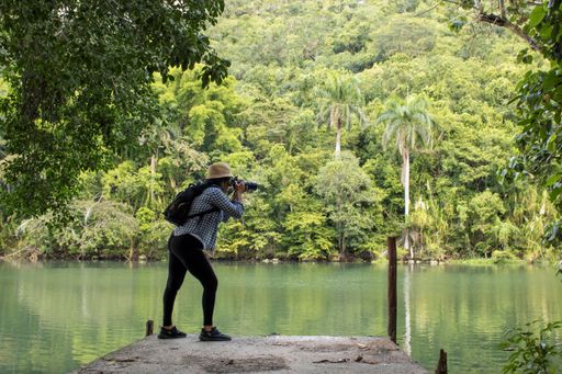 A young Hispanic female tourist taking a picture of a beautiful lake with a digital camera