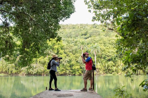 Two Hispanic tourists by the lake photographing each other with their digital cameras during the daytime