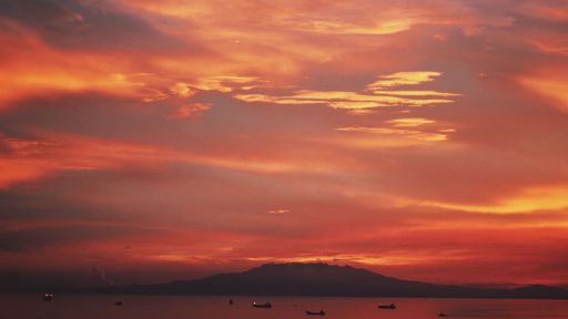 A beautiful shot of hills and the sea with boats under the beautiful red aesthetic sunset