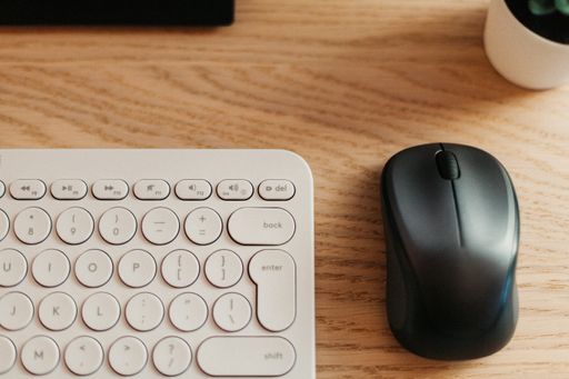 A top view of an office with a white keyboard desk and a black mouse on a wooden table