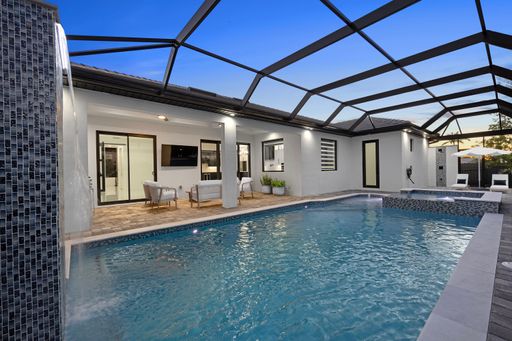 Modern outdoor pool area with seating and water feature under a screened enclosure at dusk.