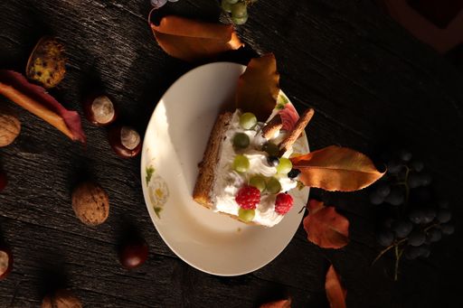 A flipped vertical shot of a creamy cake with berries, grapes, nuts, and autumn leaves