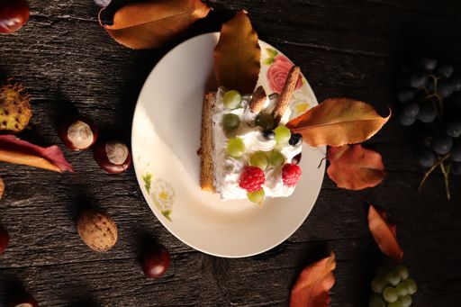 A flipped vertical shot of a creamy cake with berries, grapes, nuts, and autumn leaves