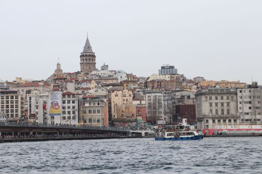 The view of Galata Tower and surrounding buildings in Istanbul with a boat on the water under a cloudy sky.