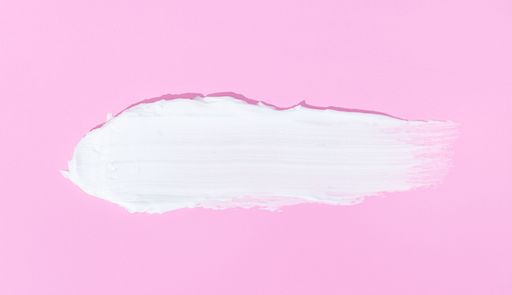 A close up of a Face or body white cream smear isolated on pink background.