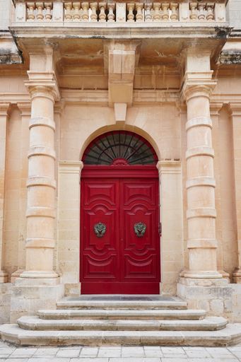 A vertical shot of a red door of a building in Mdina, Malta