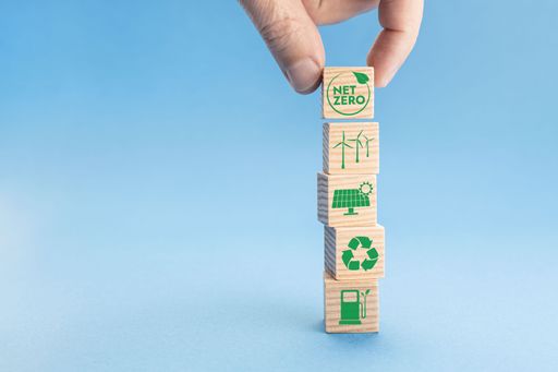 A net Zero and Carbon Neutral Concept. Hand putting wood block with Net Zero icon on top of others with green energy icons. Blue background.