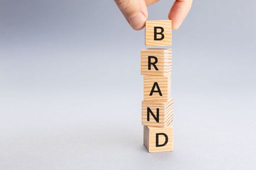 A hand arranging wooden cubes to spell BRAND word.