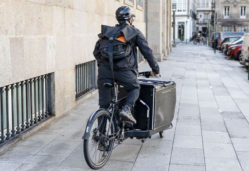 A rear view of Courier man riding a cargo bike along the city on his way to deliver a package.