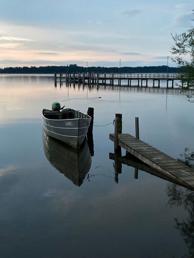 Serene evening scene of a boat docked on calm waters with a pier in the background under a peaceful sky.
