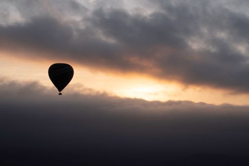 A silhouette of a single parachute against dark dramatic cloudy sky