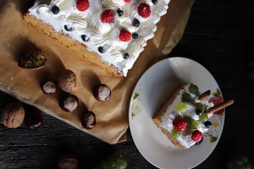 A flipped vertical shot of a creamy cake with berries, grapes, and nuts on a black surface