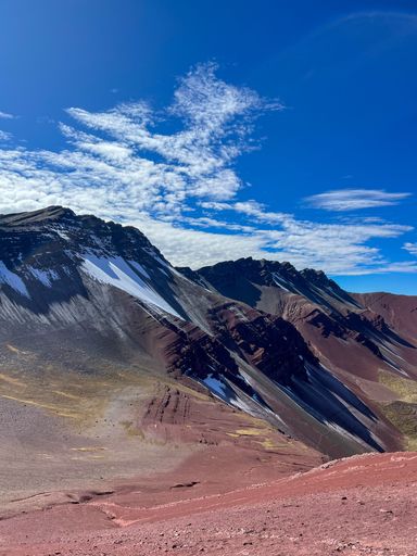 A stunning view of the Rainbow Mountain in Peru under a vibrant blue sky with scattered clouds.