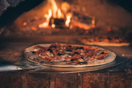 A selective focus shot of freshly baked pizza with burning firewood on background