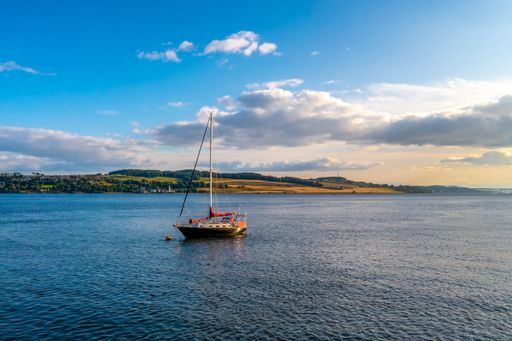 A beautiful scenery of a small sailboat on the river and a cloudy sky, Tay in Scotland
