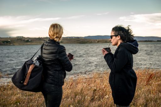 The Caucasian and Hispanic females standing against the seascape and drinking yerba mate in Argentina