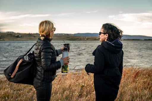 The Caucasian and Hispanic females standing against the seascape and drinking yerba mate in Argentina