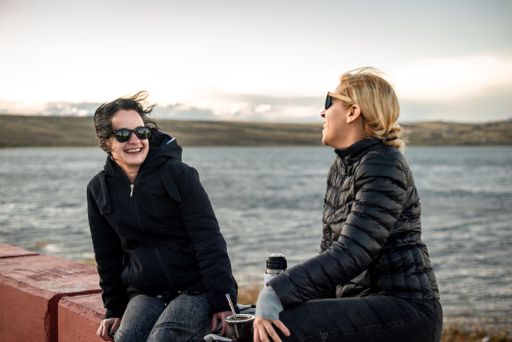 The Caucasian and Hispanic females with jackets and sunglasses, sitting on the beach on a windy day in Argentina