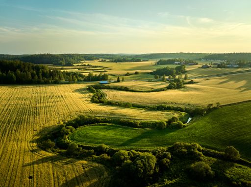 Aerial view of a serene rural landscape with fields and forests under a clear blue sky, showcasing the beauty of nature.