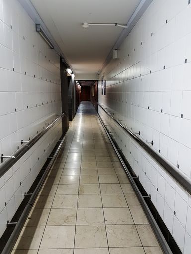A vertical shot of a white creepy hospital hallway with a ceramic floor and walls