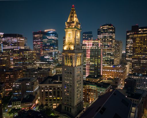 Boston's Custom House Tower illuminated at night, surrounded by skyscrapers, showcasing the city's vibrant cityscape.