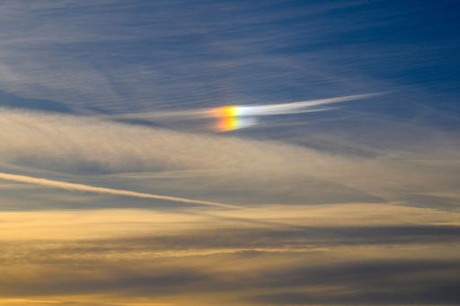 A vibrant sundog in a partly cloudy sky during sunset, showcasing a spectrum of colors against a serene backdrop.