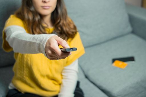 Pretty young woman sits on couch and switches on the TV.
