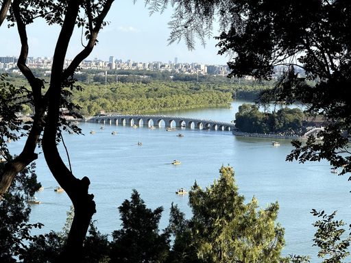A scenic view of the Seventeen-Arch Bridge at Summer Palace in Beijing, framed by trees