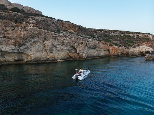 A small boat on clear blue waters near rocky cliffs under a bright sky, showcasing a serene coastal landscape.