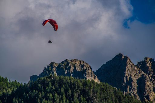 A mesmerizing view of a red paragliding over rocky mountains in hautes alpes in France with a cloudy sky