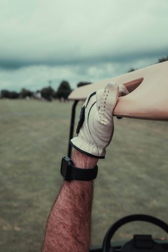 A vertical shot of a hand holding on to a golf cart