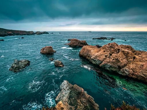An aerial shot of huge rocks in the sea with the horizon in the background under cloudy skies