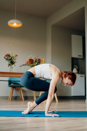 A young Caucasian female doing yoga on a rug at home
