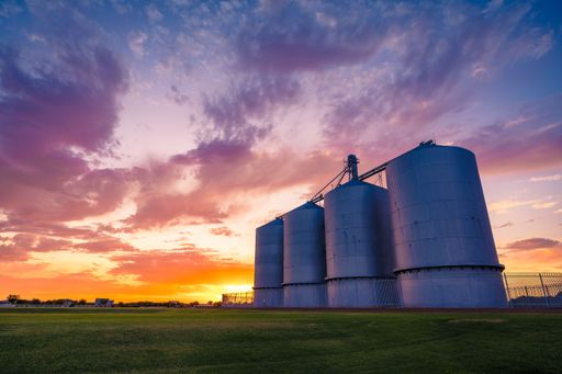 Industrial silos at sunset with vibrant sky and green field, showcasing a serene rural landscape.