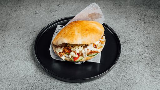 A closeup shot of a tasty burger with sauce and veggies served on a black plate