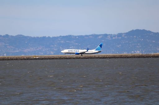 A passenger jet featuring blue-and-white livery taxis near the control tower at an airport.