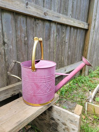 A vertical shot of a broken vintage garden pitcher in pink and golden colors