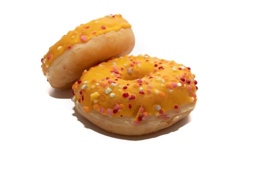 Two freshly baked orange donuts decorated with colorful sprinkles isolated on white background