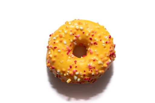 A top view of a freshly baked orange donut decorated with colorful sprinkles isolated on white