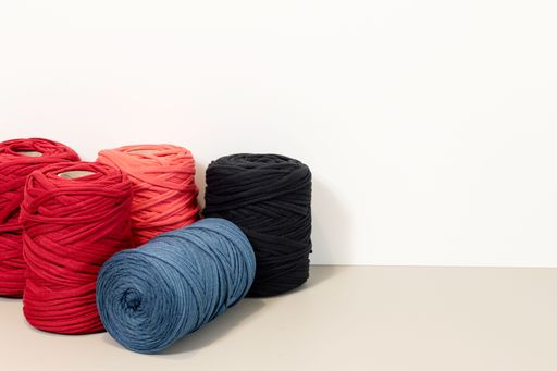 Background of a group of Spools of recycled t-shirt yarn arranged on a beige table against a white wall. Copy space
