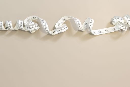 Flat lay of White measuring tape creating a border on a beige background, ideal for weight loss, diet or tailoring. Copy space