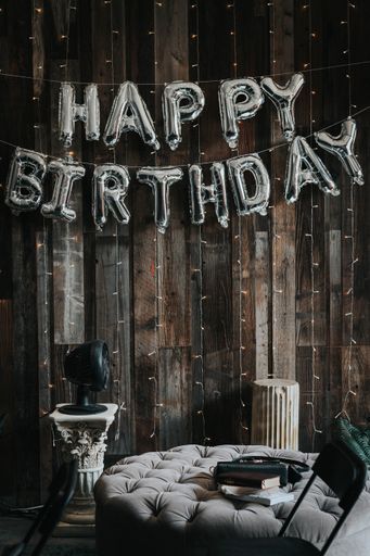 A silver "Happy birthday" balloon arrangement on a wooden wall